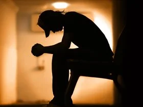 silhouette of a man sitting down with his hands on his elbows looking sad